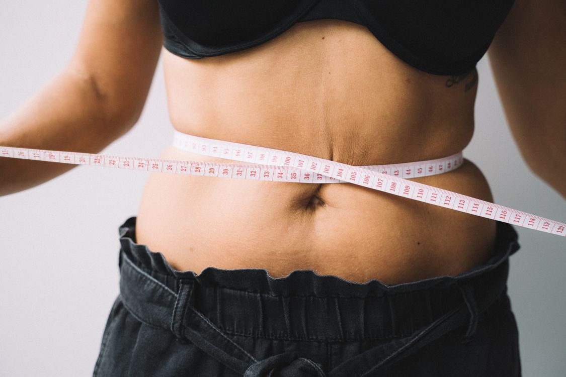 Person measuring their waist with a measuring tape to track fitness progress